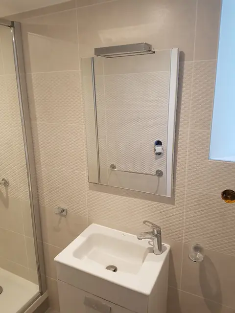 Vasque et miroir devant un mur en mosaïque beige